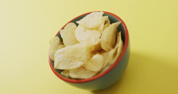 Close up of potato chips in a bowl with copy space on yellow surface alt