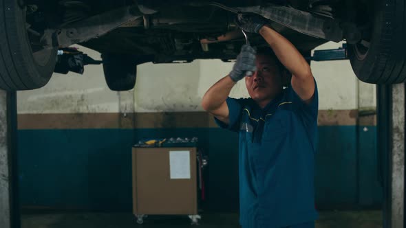 Skillful Asian guy in uniform fixing car at mechanics garage at night. alt