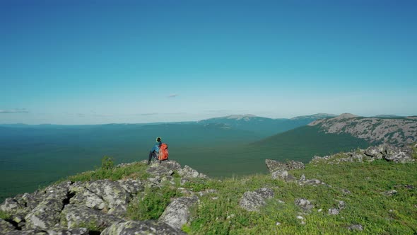 Aerial View of Young Traveller on the Mount Edge with Red Backpack alt