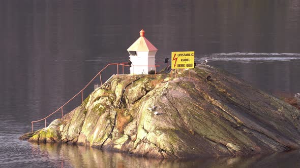 Two great cormorants drying their wings on a lighthouse island in western Norway while another cormo alt