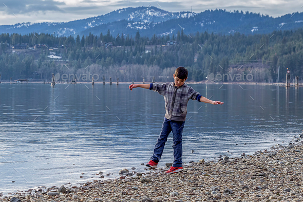 Boy spins around by lakefront.