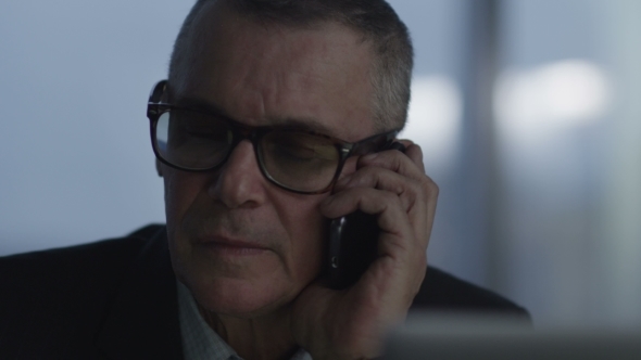 Busy Elderly Businessman Speak At Phone And Working With Computer In Modern Office alt