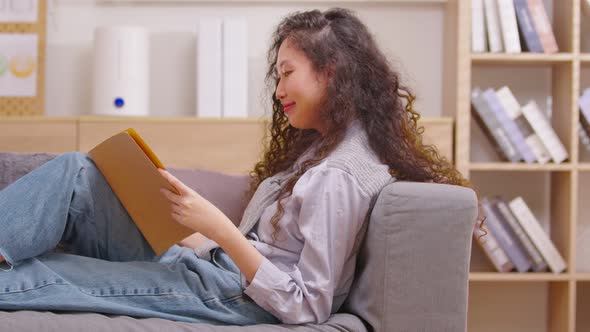Young woman reading book while relaxing with pleasure on the couch in the living room. Concept of le alt