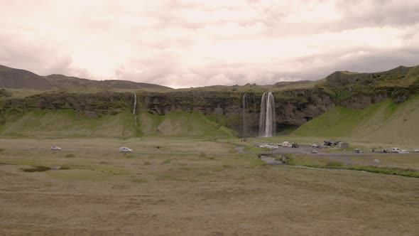 Aerial view of cars and people at the Seljalandsfoss waterfall,  in cloudy Iceland - low, approachin alt