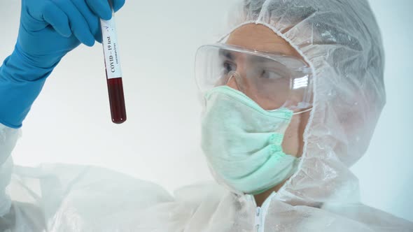 Scientist male wear protective suit, face mask, hold in hand covid-19 negative blood test tube alt