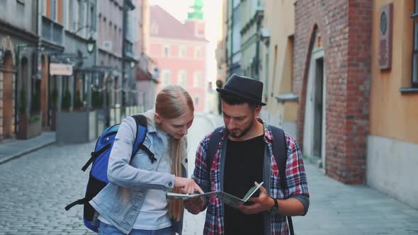 Two Young Tourists Checking Map While Walking on Main Tourist Street alt