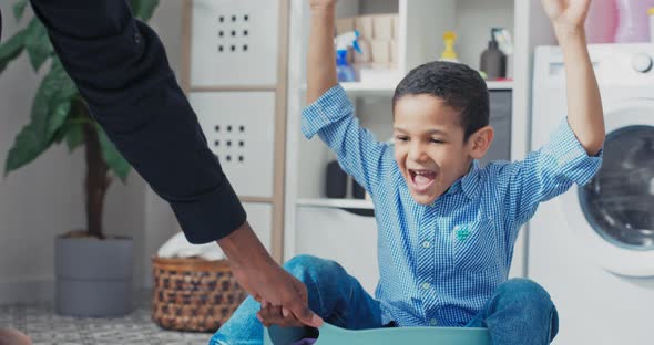 A Cheerful Little Boy with Dark Hair and Brown Eyes Sits in a Plastic Blue Clothes Bowl alt