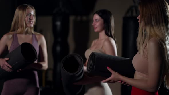 Side View Confident Young Woman Talking with Blurred Friends Standing with Exercise Mat in Gym alt