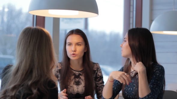 Twins Talking With a Friend While Looking At Each Other In Cafe