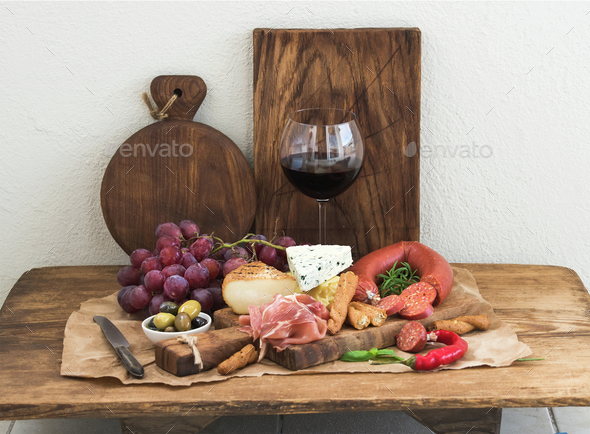 Glass of red wine, cheese and meat board, grapes, fig, strawberries, honey, bread sticks