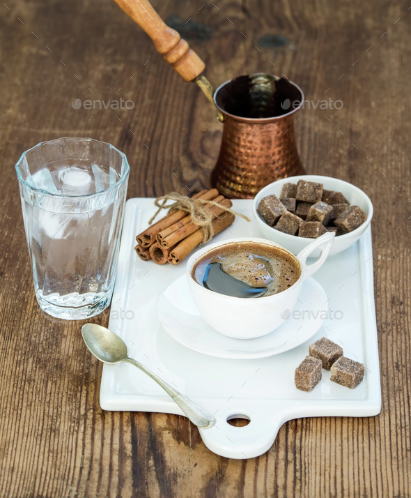 Cup of black coffee, copper pot, water with ice in glass, cinnamon sticks and cane sugar cubes