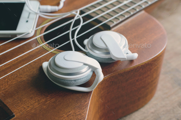 Ukulele guitar with earphone on wooden table
