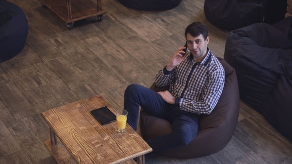 Attractive Man Sitting And Talking On The Phone On The Table Plate, a Man Smiling. alt