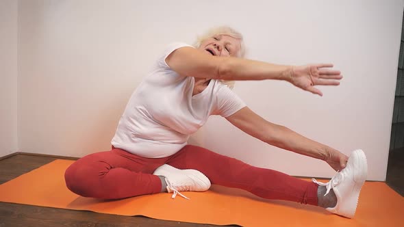 Elderly Woman Doing Stretching Exercises on the Carpet in the Living Room of the House alt