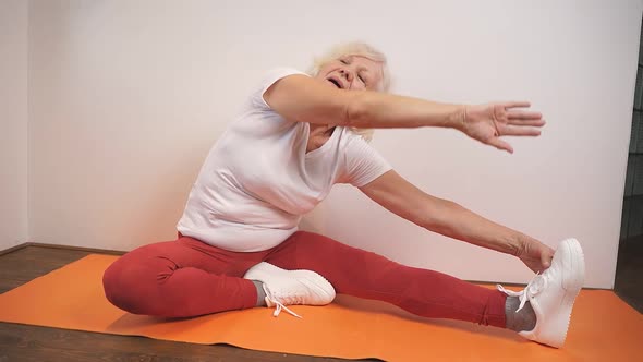 Elderly Woman Doing Stretching Exercises on the Carpet in the Living Room of the House
