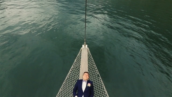 Cheerful Groom Lying In a Hammock On The Yacht And Happily Smiling