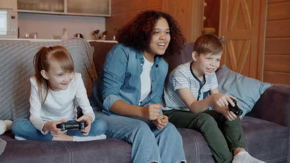 Joyful Young Babysitter Cheering Kids Playing Video Game Having Fun in Apartment alt