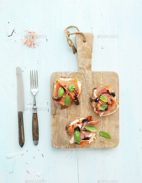 Bruschettas with Prosciutto, roasted melon, soft cheese and basil on wooden serving board
