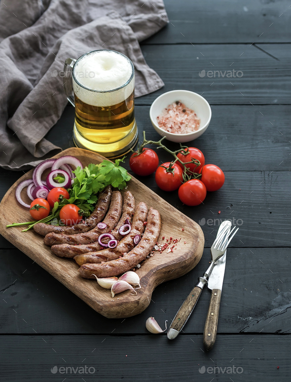 Grilled sausages with vegetables on rustic serving board and mug of light beer