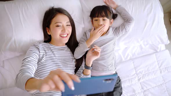 Close up of  young asian mother and her daughter making a selfie or video call. alt