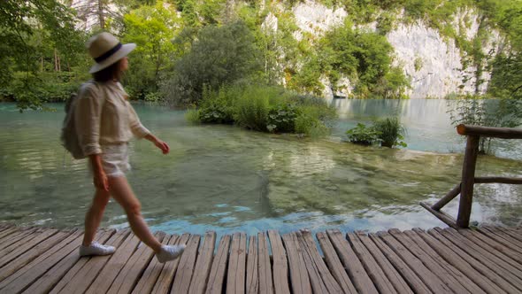 Attractive tourist in a hat walking along a wooden path along the lake. Plitvice Lakes alt
