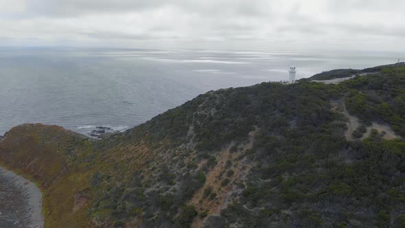 Aerial of a lonely lighthouse on top of a high cliff overlooking a big ocean on a dark stormy day. alt