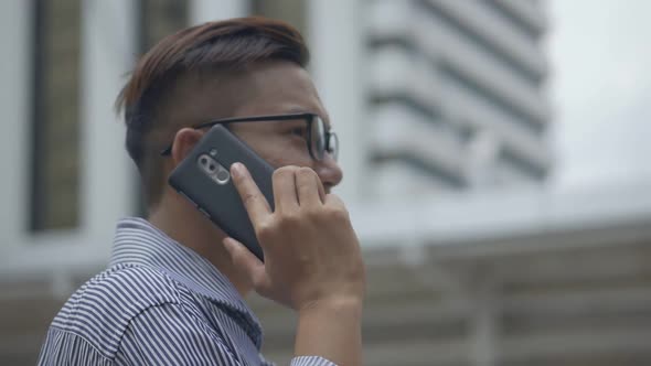 Asian men with glasses use phones in street near a big office building.