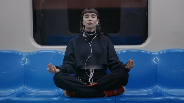 Woman Sitting in Lotus Position at Subway and Meditating alt