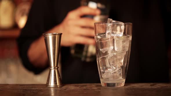 Bartender pouring double shot of vodka over ice in cocktail shaker alt