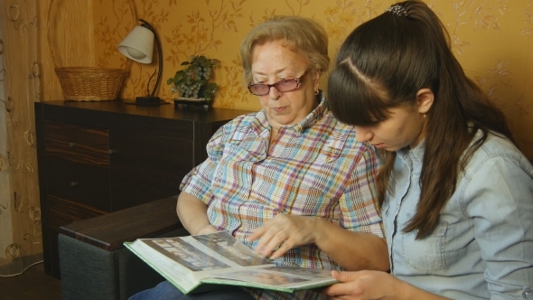 Old and Young Woman Looking at Family Photo Album on Sofa at Home alt