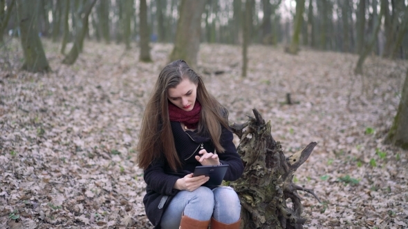 Beautiful Girl Sitting On a Stump And Using Tablet.  alt