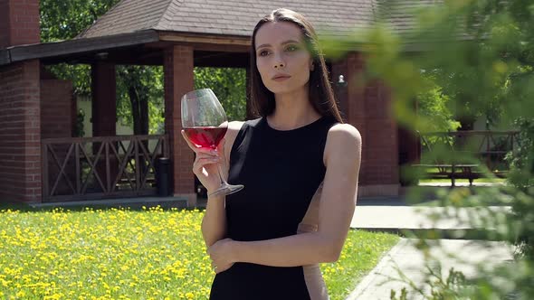 Elegant Woman with Glass of Wine Walking in Garden of Mansion alt