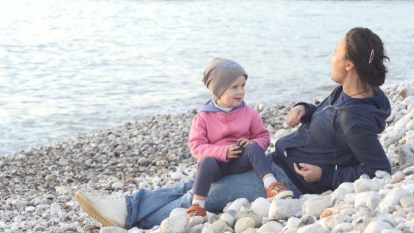 Mother And Child Sit On The Beach And Enjoy The Sunset alt