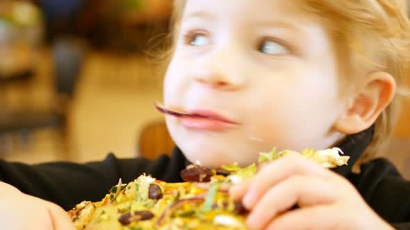 A Young Blond Boy Devours A Pizza Slice.