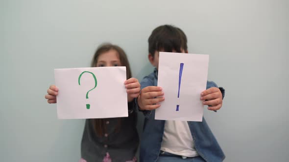A Boy and a Girl Smile and Hold Pieces of Paper with an Exclamation Mark and a Question Mark