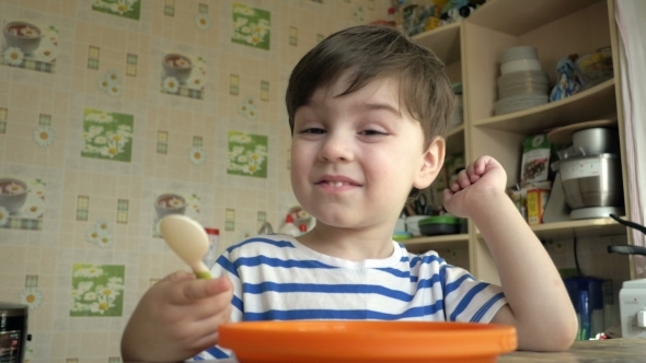 A Little Boy Alone Eating Porridge In The Afternoon, In The Kitchen.