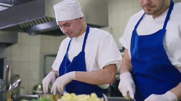Positive Man Talking Mixing Salad in Bowl and Smiling Looking at Camera Standing with Unrecognizable alt