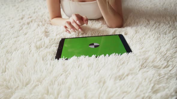 Woman is Lying on Carpet with Tablet with Chromakey Screen and Swipe Her Finger on Touch Screen alt