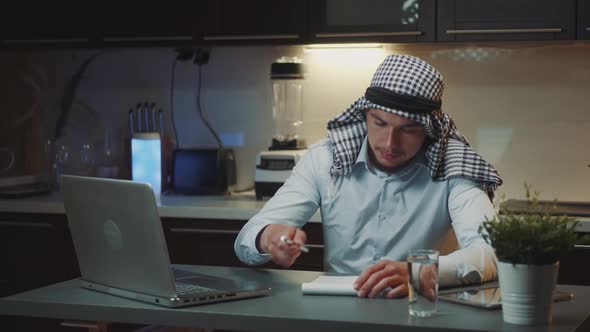 Arabic Young Man Using Laptop and Notebook While Having a Remote Work