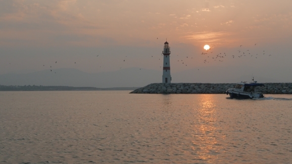 Boats Passing Lighthouse With Rising Sun