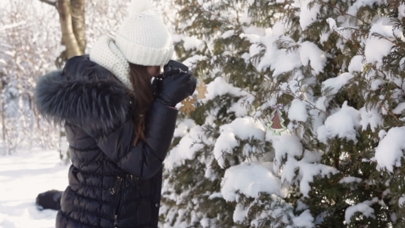 Beautiful Young Woman In Winter Clothing And Knitted White Hat Photographing Snowy Forest