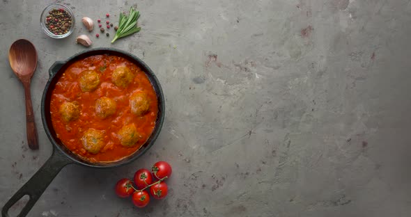 Cooking meatballs with tomato sauce in black pan alt