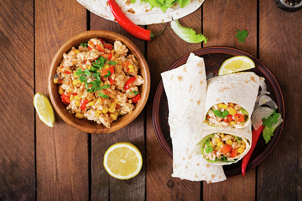 Burritos wraps with chicken meat, corn, tomatoes and peppers on wooden background. Top view