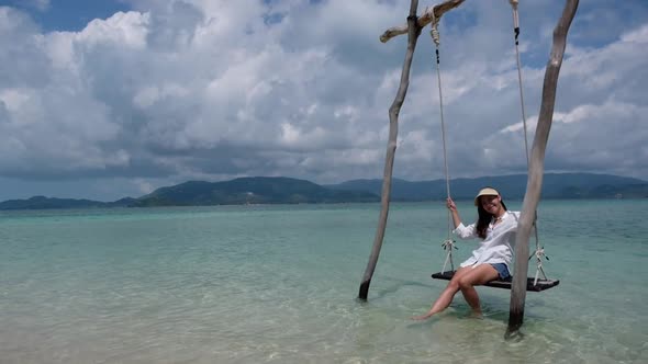 Slow motion of a beautiful young asian woman sitting on swing in the sea