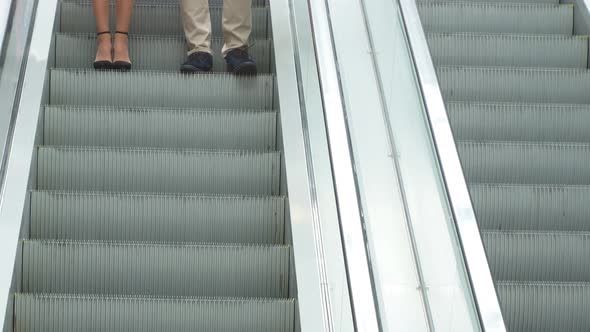 Young Fashionable Family Riding an Escalator in a Shopping Center with Bags in Their Hands. alt