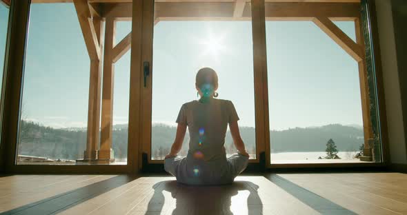 Meditating Girl in Pajamas Sits in Lotus Pose at Home By Window with Epic View