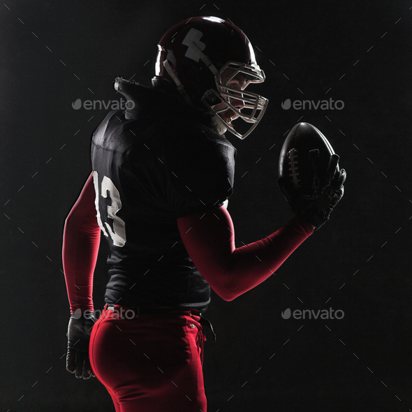 American football player posing with ball on black background - Stock Photo - Images