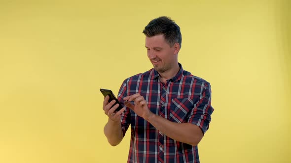 Cheerful Young Man is Very Delighted with Something Looking on Smartphone alt