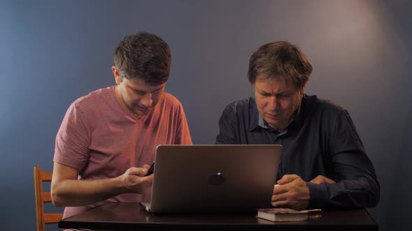 Man with Phone Shows How To Input Data To Senior Father alt