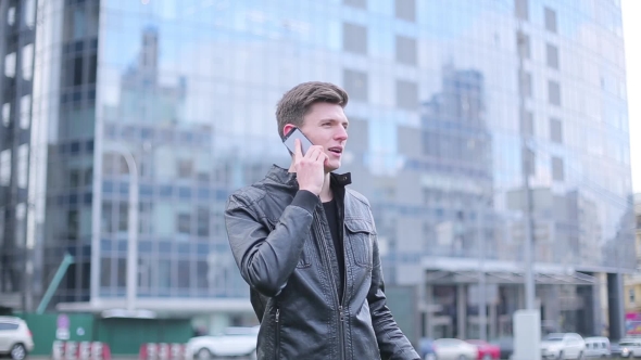 Brunette Guy Talking On a Mobile Phone On The Background Of The Business Center